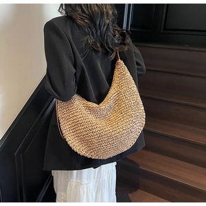 Close-up of a large hand-woven hobo bag with brown leather strap worn by a model