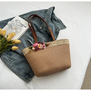 Handcrafted straw tote bag with lace trim and floral accents on a denim jacket background
