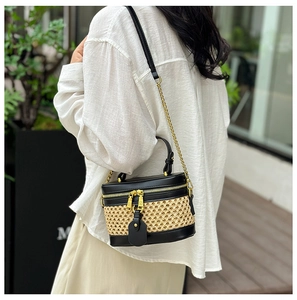 Detail view of woven straw bucket bag with black leather trim and golden chain strap