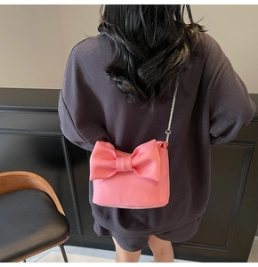 Close-up of pink bow crossbody bag with silver chain strap worn by a model