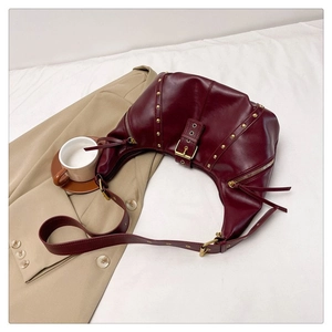 Détail d'un sac hobo bordeaux avec rivets dorés et boucles métalliques sur tissu kaki
