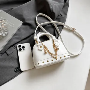 Weiße Mini-Muscheltasche aus Kunstleder mit Goldnieten-Boden und Kettendekor auf Tisch