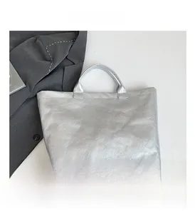 Detail of silver metallic tote bag featuring wrinkled texture and white TOTE BAG lettering