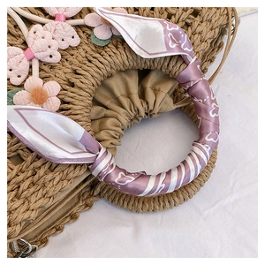 Detailed macro view of woven straw bag handle with purple silk scarf and floral decor
