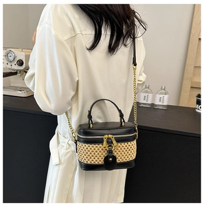 Detail of woven straw and black leather box bag with gold chain strap on model