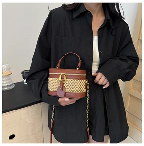 Detail of a mini cylinder straw vanity bag featuring brown leather trim and gold chain strap