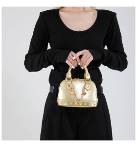 Detail der goldenen Muscheltasche mit Metallkette und Nieten auf schwarzem Outfit