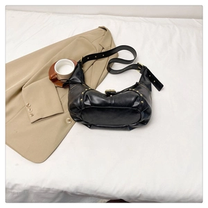 Gros plan d'un sac hobo vintage en cuir noir avec rivets dorés sur un fond blanc doux