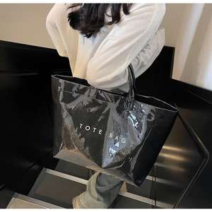 Sac fourre-tout noir brillant avec texte blanc TOTE BAG porté par un mannequin en extérieur