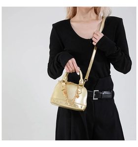 Detail einer goldglänzenden Muscheltasche mit Nietenbesatz und Kettenelementen