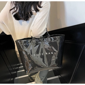 Gros plan d'un sac cabas noir brillant avec inscription TOTE BAG blanche porté par un mannequin