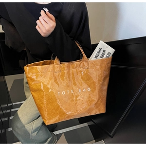 Détail d'un sac cabas marron texturé avec imprimé TOTE BAG présenté dans un décor urbain