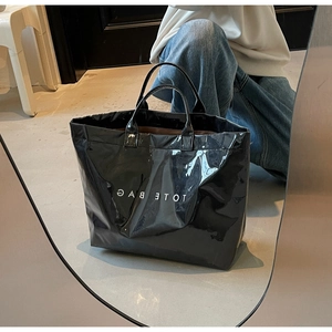 Détail d'un sac cabas en cuir verni noir avec texte TOTE BAG blanc et fini brillant