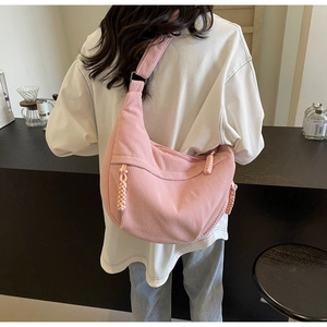 Pink corduroy crescent shoulder bag with woven zipper detail and wide strap worn by model