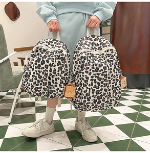 Detail view of large and small leopard print canvas backpacks with cute plush pendants