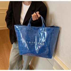 Détail du grand sac cabas bleu foncé brillant avec texte blanc tenu par la main