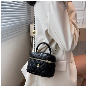 Detail of black quilted mini box bag with gold floral clasp and chain strap on a white suit