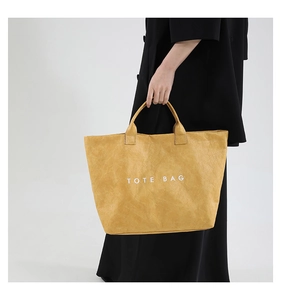 Detail of yellow Tyvek tote bag featuring a crinkled texture and white TOTE BAG print