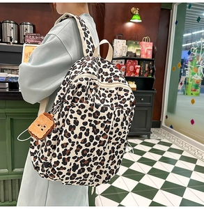 Detail of leopard print canvas backpack with cute plush bear charm in a cafe setting