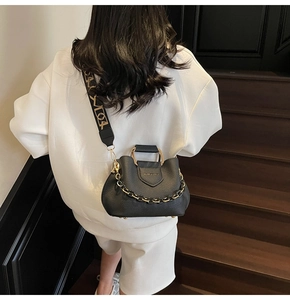 Detail of black lychee grain leather bucket bag with wide patterned strap and gold chain