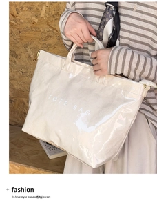 Close-up of cream glossy leather tote bag with white text held by model outdoors