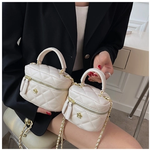 Close-up of a cream quilted mini box bag featuring a gold camellia flower and chain strap