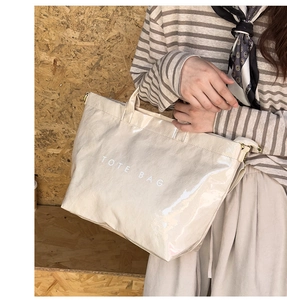 Close-up of cream glossy tote bag with white text and gold metal ring detail