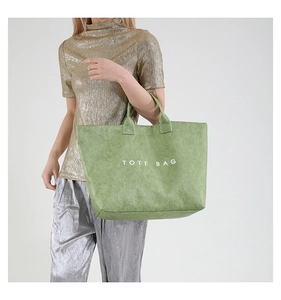 Detail of green textured tote bag with white lettering held by a fashion model