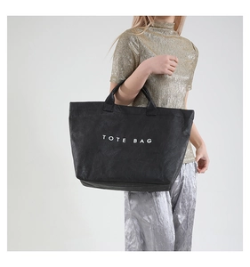 Detail of minimalist black tote bag with white text print on wrinkled texture material