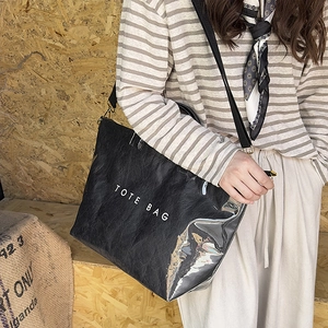 Detail view of black textured tote bag with white text and adjustable shoulder strap