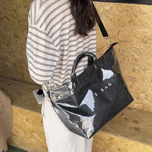 Side view of model wearing a black glossy tote bag with adjustable shoulder strap