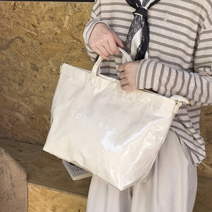 Detail of a creamy white glossy tote bag with dual handles and metal attachment ring