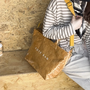 Macro detail of the glossy brown tote bag with yellow strap on a casual model