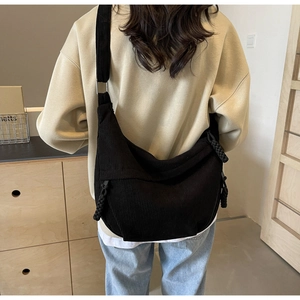Close-up of black corduroy crossbody crescent bag featuring wide strap and braided zip puller