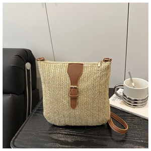 Detail of woven straw crossbody bag with brown leather strap on a wooden table