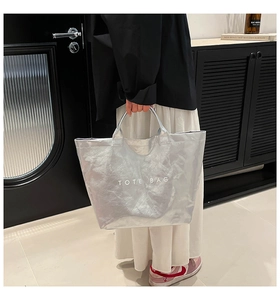 Detail showing metallic silver crinkled texture tote bag with white TOTE BAG print