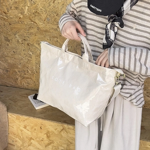 Close-up of a cream-colored glossy tote bag with white TOTE BAG text print detail
