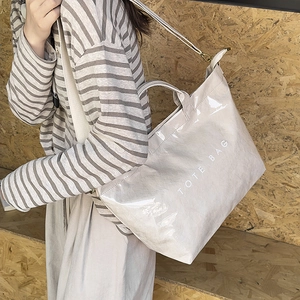 Close-up of beige glossy tote bag with white text and adjustable shoulder strap