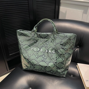 Retro green snake pattern tote bag with white text print on a black leather sofa