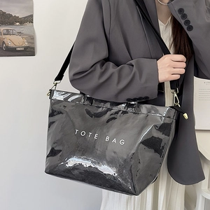 Detailed view of a high-gloss black tote bag with white lettering and woven shoulder strap