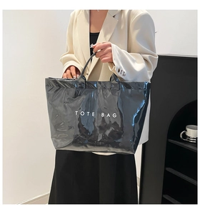 Glossy black tote bag with white TOTE BAG print worn with a chic beige blazer