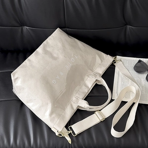 Chic beige crinkled tote bag with shoulder strap displayed on a luxury black leather sofa