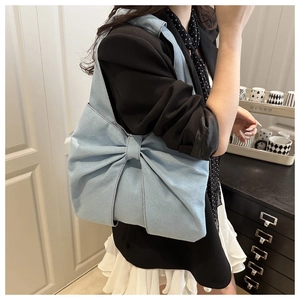 Detailed close-up showing texture of light blue denim shoulder bag with a large bow design