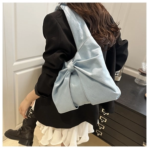 Sac à épaule en jean bleu avec un grand nœud décoratif porté par un mannequin
