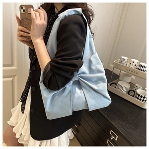 Detailed shot of a light blue denim tote bag with a large bow held by a model