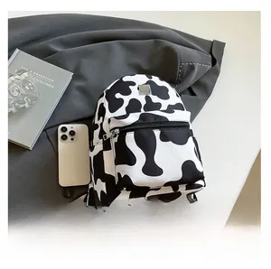 Mini cow print backpack featuring stylish black and white patterns next to a phone for scale