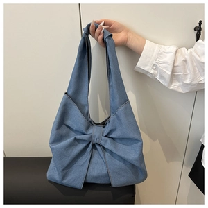 Detail of light blue denim hobo bag featuring a large decorative bow and soft pleated fabric