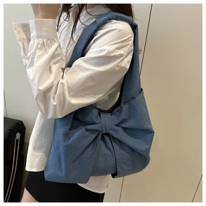 Détail du sac à épaule en jean bleu avec un grand nœud décoratif et texture souple
