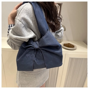 Detailed view of dark blue denim tote bag featuring a large decorative bow and sturdy strap