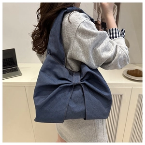 Détail du sac bandoulière en jean avec nœud porté par un mannequin en intérieur